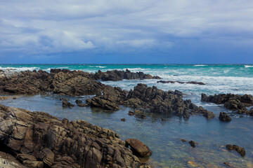 Rocky shoreline with vibrant ocean waters under a cloudy sky in South Africa