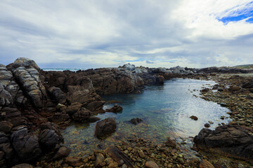Coastal rock formations and tranquil waters in South Africa under an overcast sky