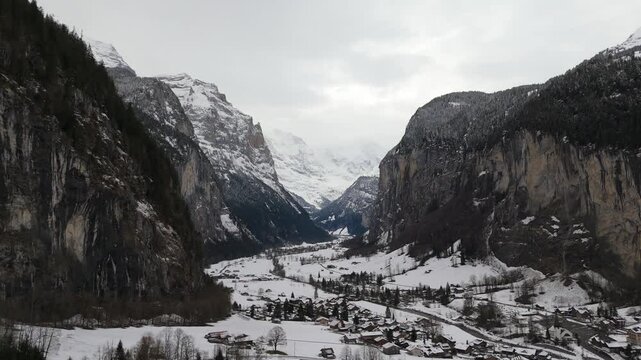 Lauterbrunnen Valley and Snowy Mountains on Cloudy Winter Day. Swiss Alps. Switzerland. Aerial View. Moving Backwards