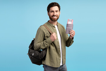 Smiling Latin young man holding passport and backpack, posing at camera in studio