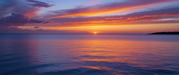 Obraz premium Stunning coastal sunset with vibrant orange and purple hues reflecting in tranquil blue waters, ideal for serene backgrounds and text overlay.