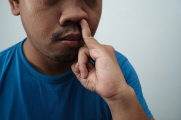 Close up of Asian brown man picking his nose with his pinky finger to find a booger
