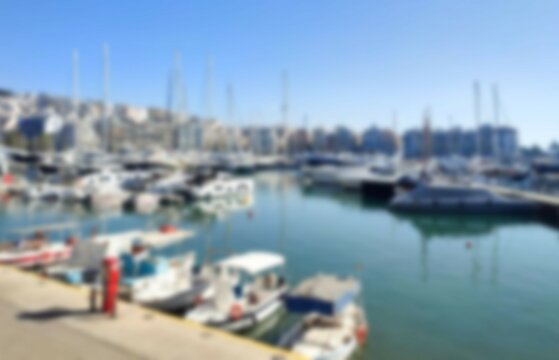 Bokeh view of yachts and sailboats moored at Marina Zeas in Pasalimani, Piraeus, Greece, with the picturesque Kastella Hill rising in the background. 