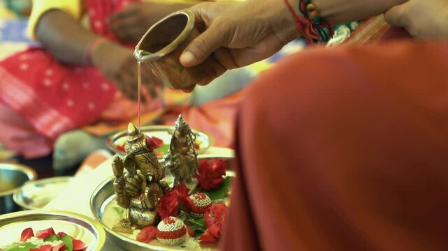man worshiping lord ganesh by offering Kalash & Water during pooja or ritual celebration at home in India.