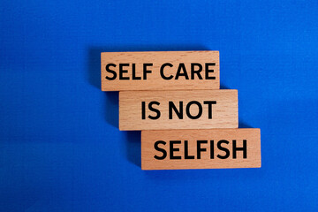 Self care is not selfish message written on wooden blocks on blue background. Conceptual self care...