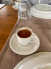 A cup of freshly brewed Turkish coffee served on a white saucer on a wooden table with neutral decor.