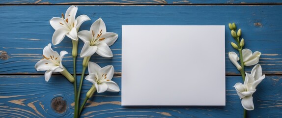 White blank card beside white Alstroemeria flowers on a blue wooden background for creative design and greeting card mockups.