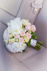 Bridal bouquet of white peonies and soft pink roses in delicate pastel shades on a beige leather car seat