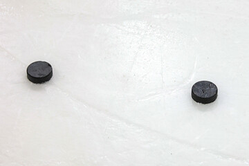 Two old black ice hockey pucks laying on ice.