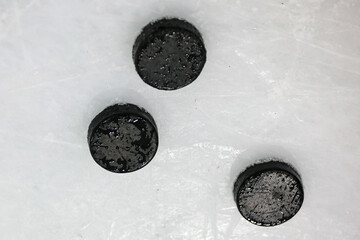 Black ice hockey rubber pucks set of 3 laying on Ice.