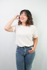 Beautiful young asian woman with wavy hair wearing white shirt is showing love heart hand gesture, isolated over white background.