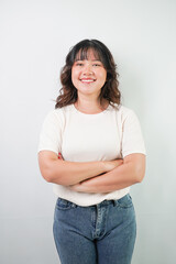 Beautiful young asian woman with wavy hair wearing white shirt is showing confident gesture, isolated over white background.