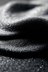 Close-up of sparkling black grainy surface with tiny reflective particles. The surface is uneven, creating a sense of depth and shadow