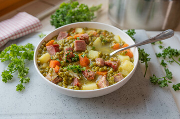 Homemade hearty pea soup with pork meat and vegetables on a plate.