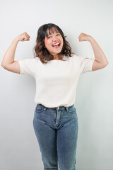 Beautiful young asian woman with wavy hair wearing white shirt is flexing her bicep muscle gesture,...
