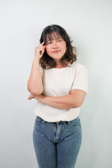 Beautiful young asian woman with wavy hair wearing white shirt is showing thinking or planning gesture, isolated over white background.