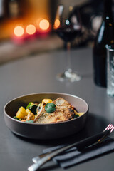 Crispy seabass fillet with roasted vegetables, creamy bisque sauce, and fresh herbs, elegantly plated in a dark ceramic bowl on a stylish minimalistic table setting