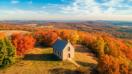 Aerial view of a small stone church nestled on a grassy hilltop, surrounded by vibrant autumn foliage, creating a serene and picturesque scene of tranquility amidst nature's beauty