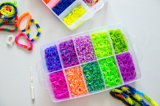 Box of colorful loom bands and bracelets on white table.