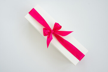 Elegant white gift box with bright pink ribbon bow on minimalistic background