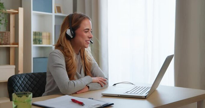 Happy businesswoman wearing headset waving and smiling during a video conference from home