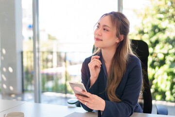 Obraz premium Close-up of a young Asian businesswoman using a smartphone while working in a bright and modern office