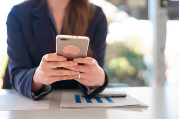 Close-up of a young Asian businesswoman using a smartphone while working in a bright and modern office