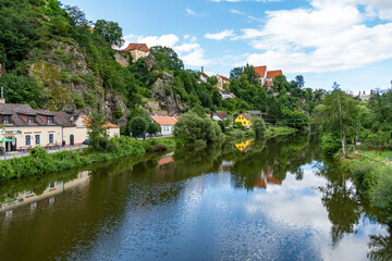The shore of the Luznice River in South Bohemia with small houses and a church on a rock above the water.