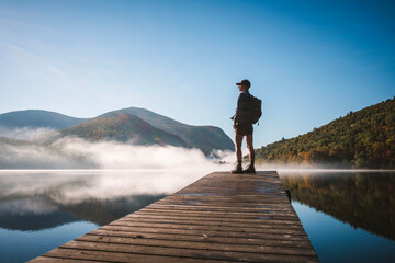 Woman stands on dock with fog, mountains on peaceful morning, Maine