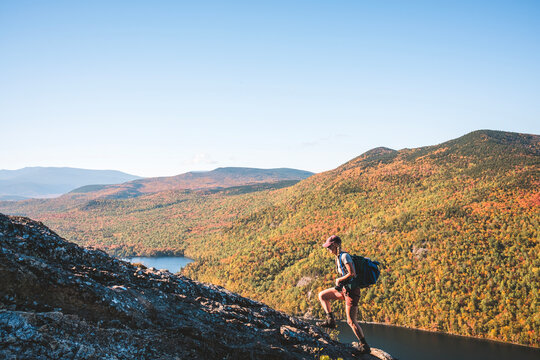 Woman hikes along mountain ridge with vibrant fall foliage, Maine
