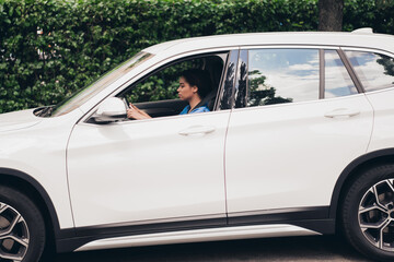 Young woman driving a white car through a vibrant urban environment on a beautiful sunny day