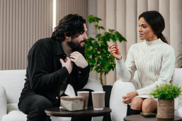African woman talks to boyfriend about relationship problem on counseling session or couples therapy. Annoyed American man sitting on chair and listening his girlfriend. Psychology concept