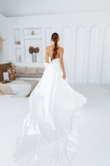 Fototapeta premium Porter from behind a young bride in a white trendy dress with a long train on a white background in the studio.