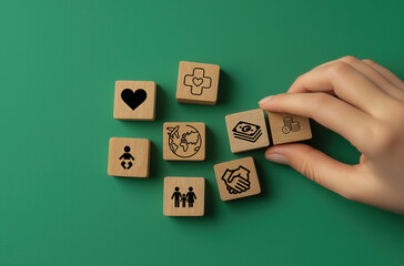 hand arranging wooden blocks with various life-related icons, including heart, healthcare, money, family, travel, and partnership symbols, on a green background
