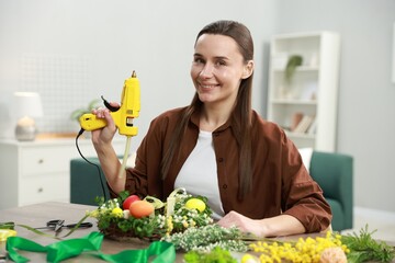 Woman with hot glue gun at table indoors
