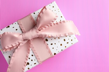 Gift box with beautiful bow on pink background, top view. Space for text