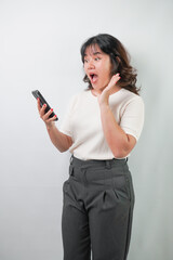 Fototapeta premium Beautiful young asian woman with wavy hair wearing white shirt is using a smartphone, isolated over white background.