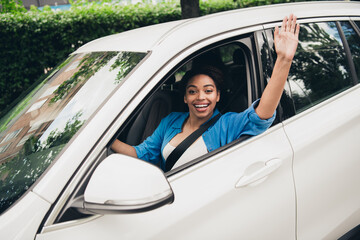 Young woman joyfully greeting from car window during sunny day in city
