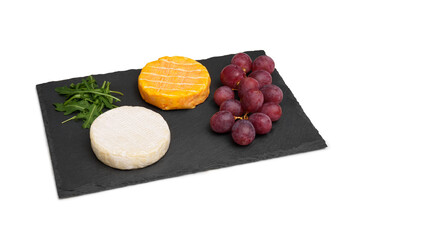 Two cheesy round heads of brie with grapes and arugula on a black slate board. A snack. Isolated cheese board on a white background.