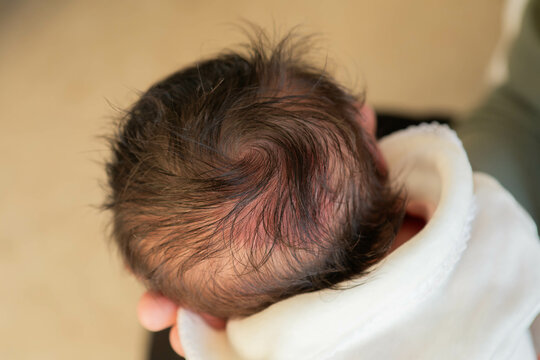 Close-up of newborn baby's head with dark brown hair and cowlick in hospital