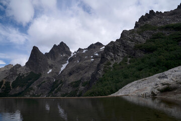 Obraz premium Alpine landscape. Panorama view of Cerro Lopez rocky mountains and the calm lagoon reflecting the environment and sky with dramatic clouds