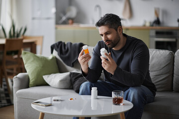 Handsome man thoughtfully considers medication while seated at stylish urban living room table
