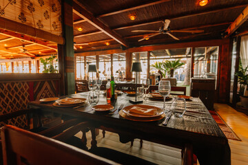  Elegant restaurant interior with a rustic wooden table set with plates, glasses, and napkins, surrounded by warm lighting and cozy decor.