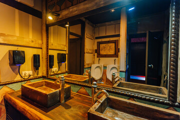 Rustic restroom with wooden sinks, mirrors, warm lighting, and vintage decor, featuring urinals and hand soap dispensers in a cozy atmosphere.