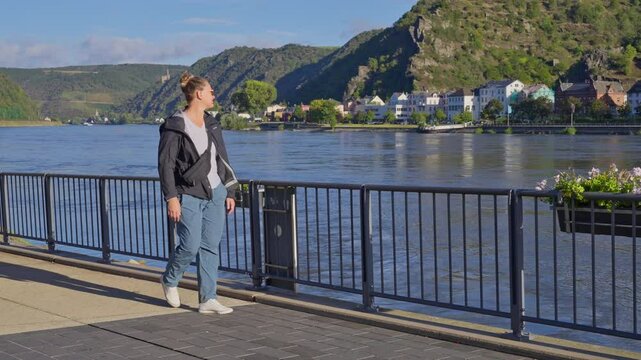 Woman strolling on the waterfront sidewalk during the early morning in the Rhine River Valley, Sankt Goar, Germany