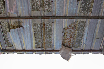 Close-up of a deteriorated corrugated metal roof, showing visible rust, peeling paint, and weathered surface.