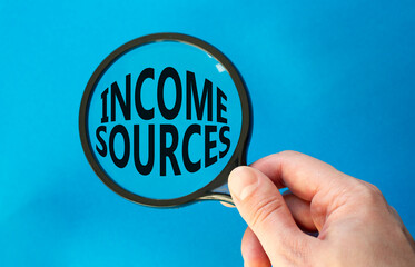 Income Sources symbol. Magnifying Glass with Concept word Income Sources. Beautiful blue background. Businessman hand. Business and Income Sources concept. Copy space