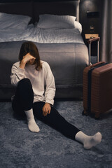 Sad woman sits on the floor, feeling overwhelmed and lonely. Female with suitcase having...