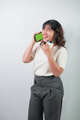 Beautiful young asian woman with wavy hair wearing white shirt holding a smartphone and coffee cup, isolated over white background.