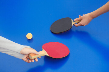 Close-up of table tennis racket and ball on table. Hands holding paddles over blue ping pong table. Sport concept. Banner